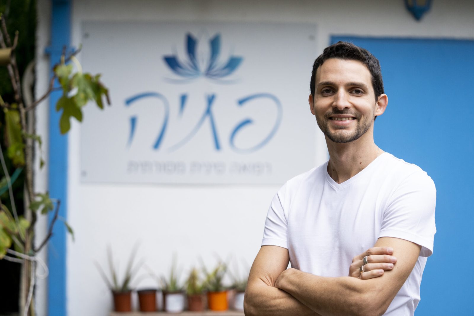 יניב פתיה עומד בכניסה לקליניקה, מתחת לשלט עם סמל הלוטוס
